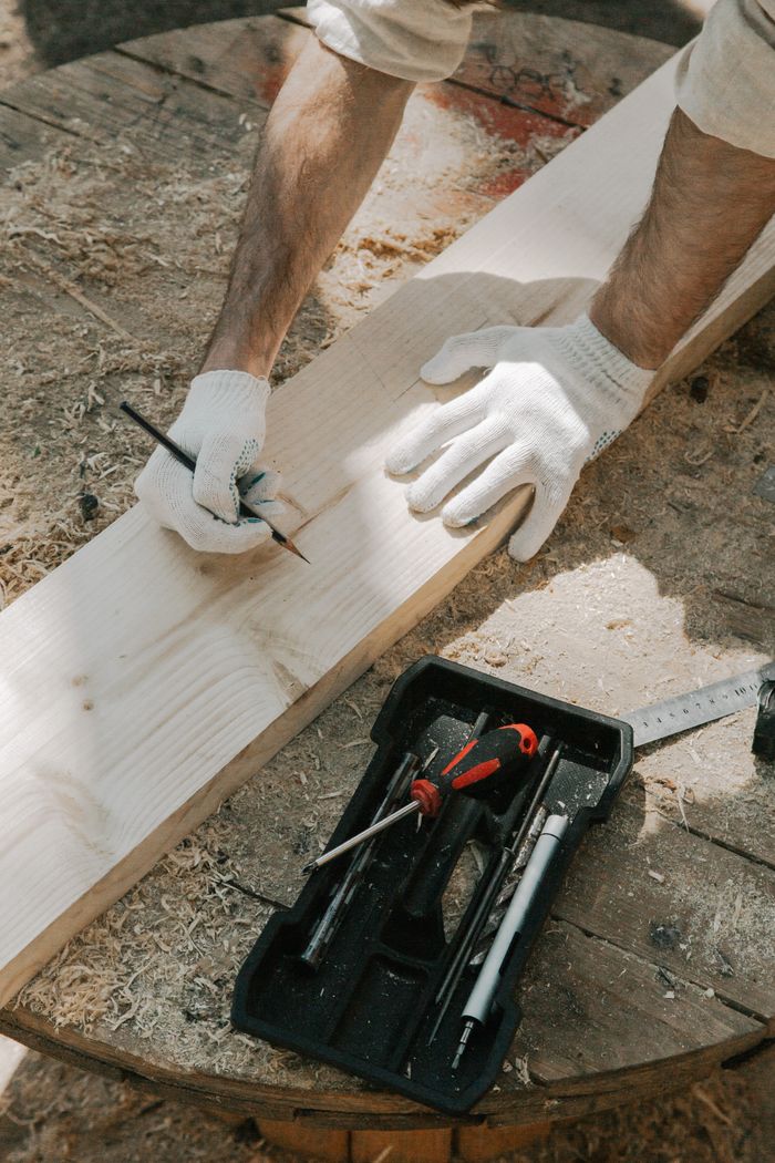 Carpenter measuring and marking wood plank with precision tools and gloves.